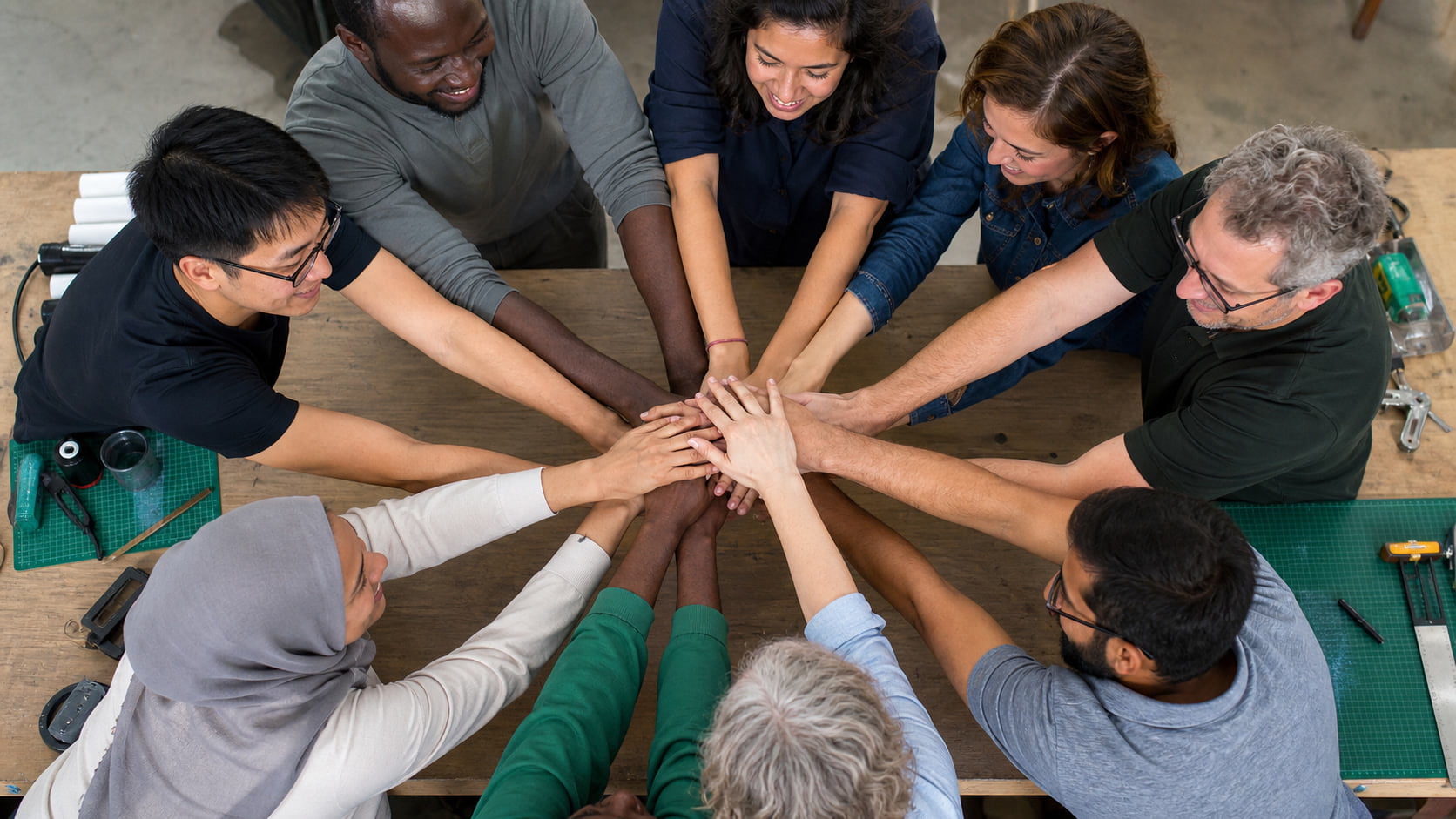A globally diverse team joining hands around a workshop table